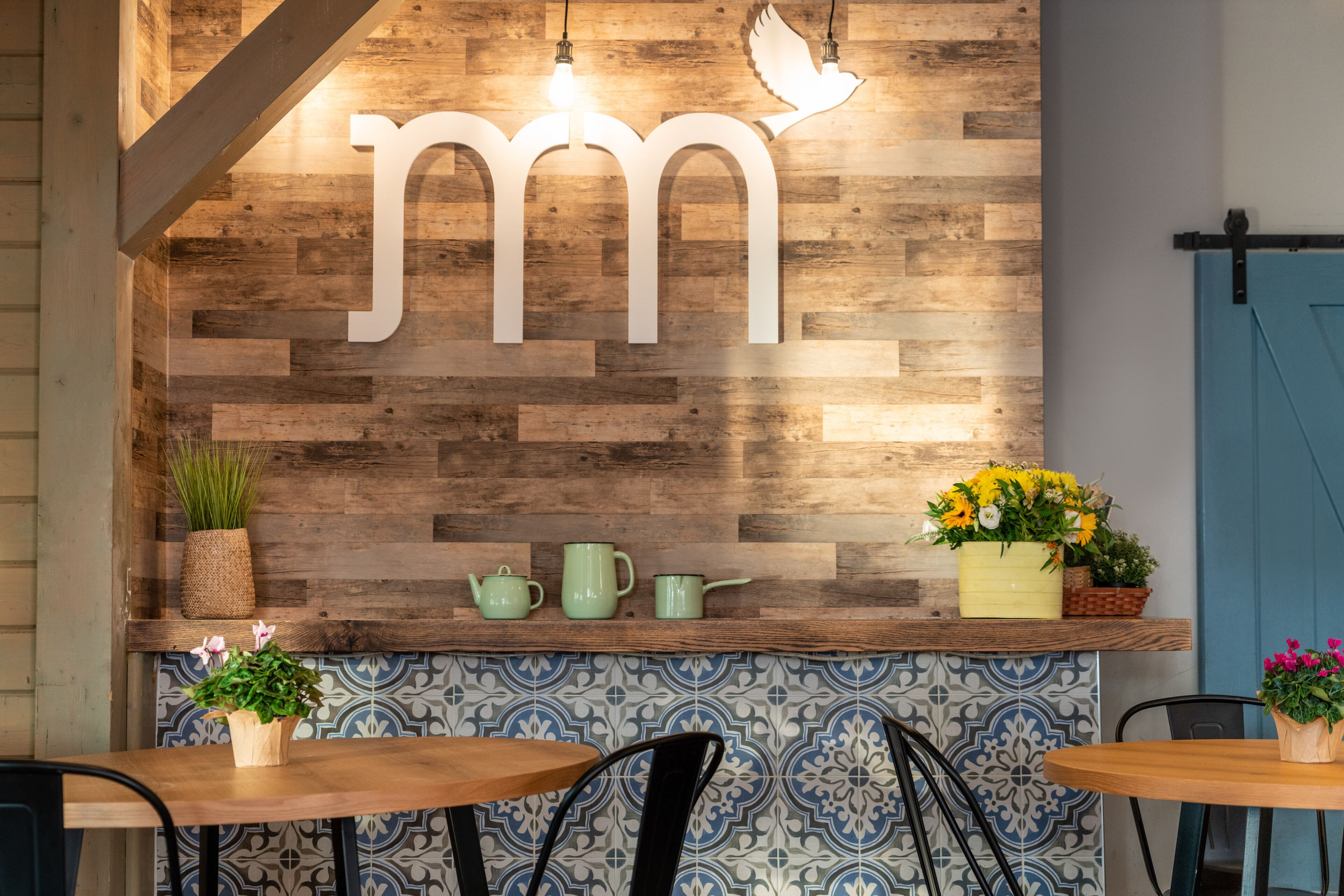 A wooden wall with a large 'm' sign, a shelf with plants and teapots, and a patterned tile backsplash.
