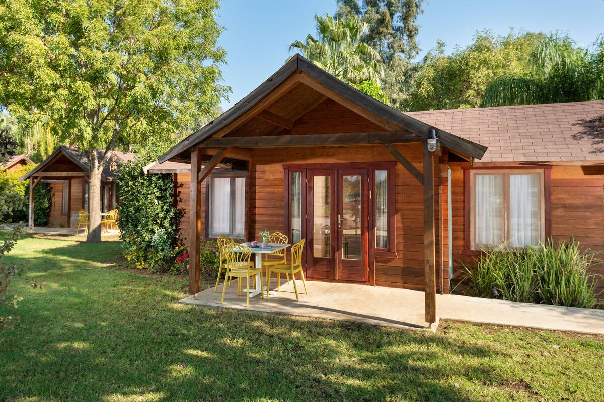 Une cabane en bois avec une véranda, une table à manger avec des chaises et un petit jardin.