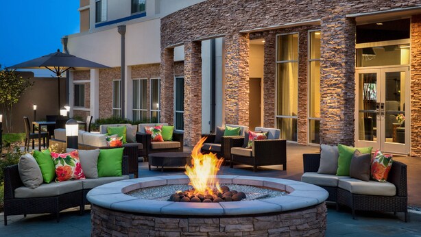 An outdoor seating area with a stone fire pit surrounded by wicker furniture and cushions.