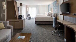 A modern hotel room with a bed, a desk, a chair, a sofa, a TV, and a lamp.