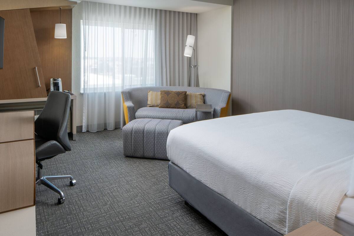 Une chambre d’hôtel avec un grand lit, un bureau avec une chaise, un canapé et un lampadaire.