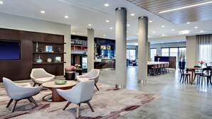 A modern hotel lobby with a bar area, seating arrangements, and a large screen.