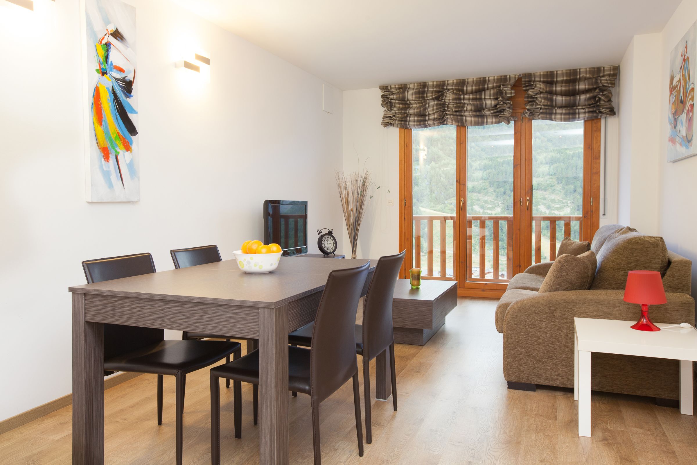 Een eetgedeelte met een houten tafel en stoelen, een fruitschaal en een klok aan de muur.