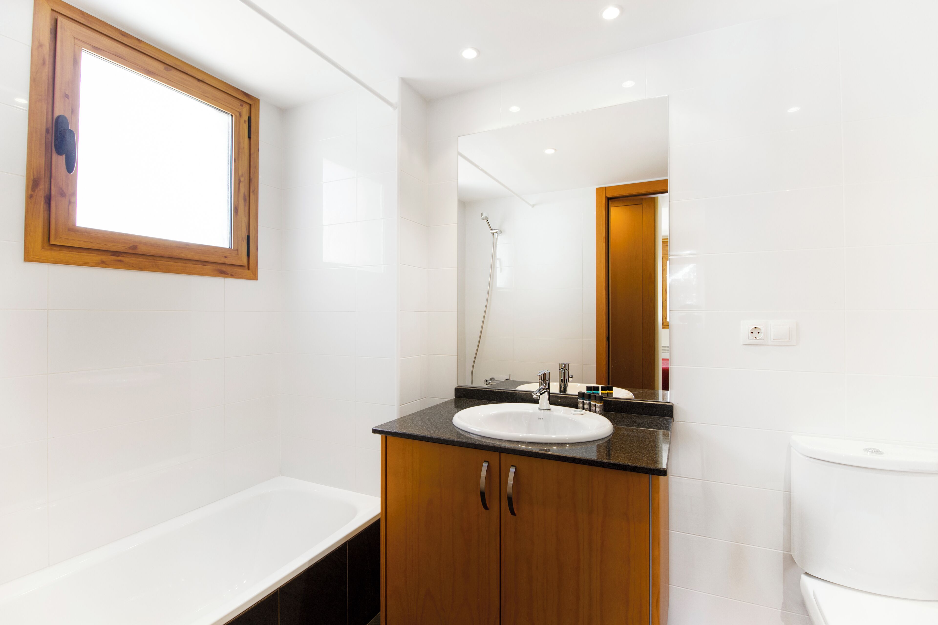A modern bathroom with a wooden vanity, white tiles, a large mirror, and a bathtub.