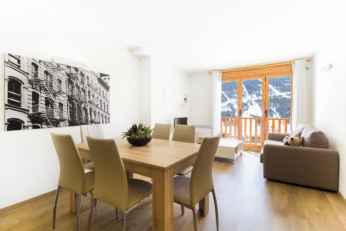 A modern living room with a dining area, a sofa, and a large window with a view of mountains.