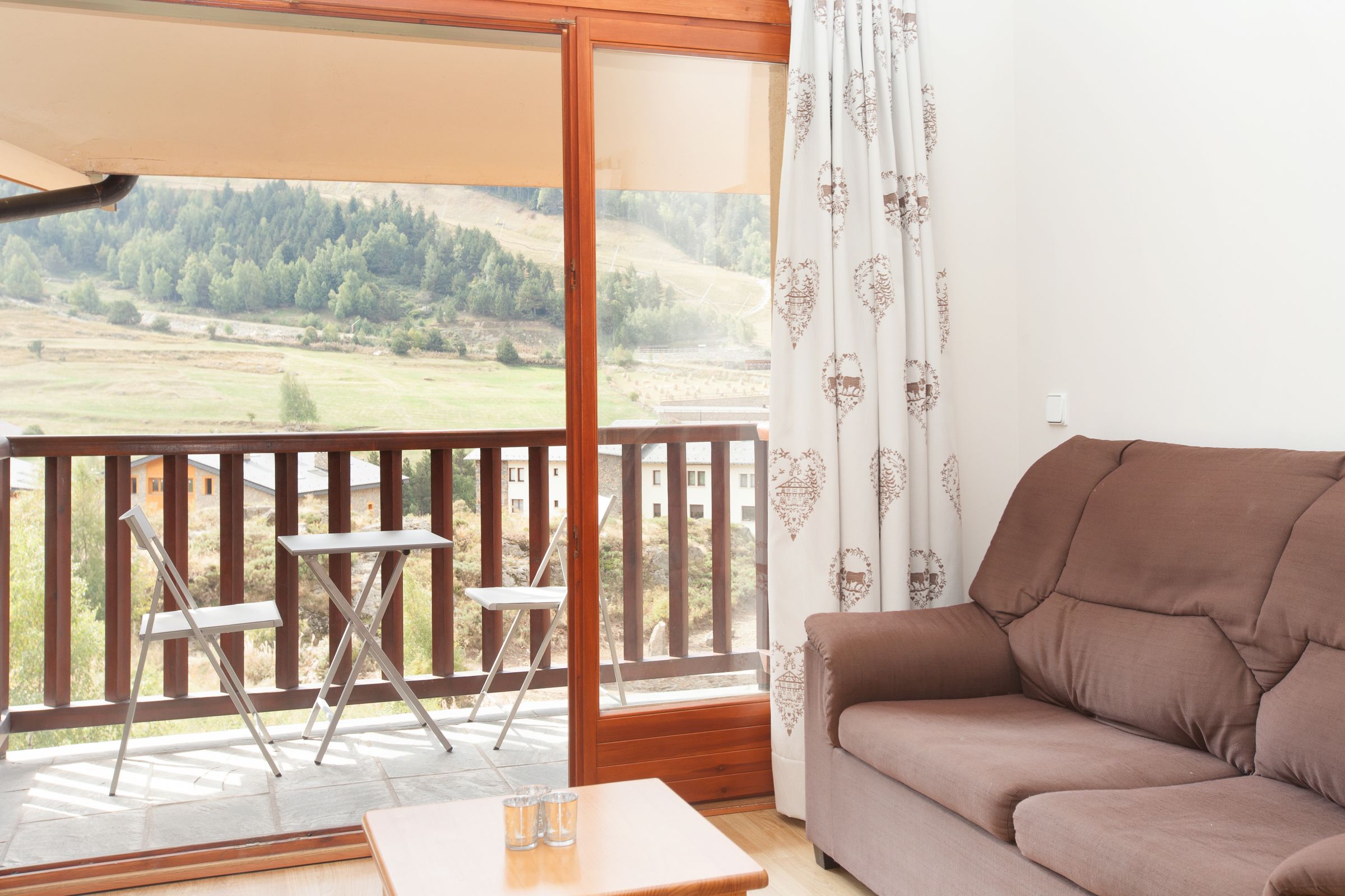 A balcony with a sofa and two chairs, overlooking a scenic landscape.