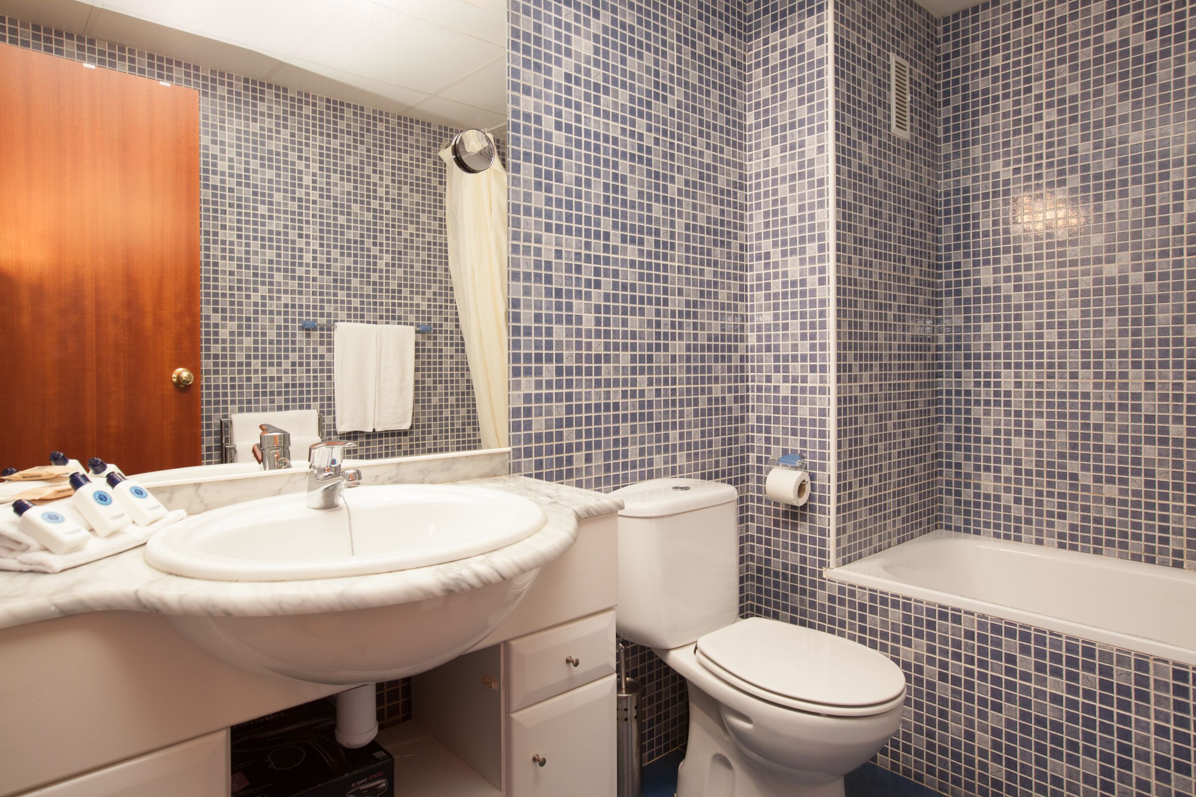 A bathroom with a white sink, toilet, and bathtub, tiled with small blue and white tiles.