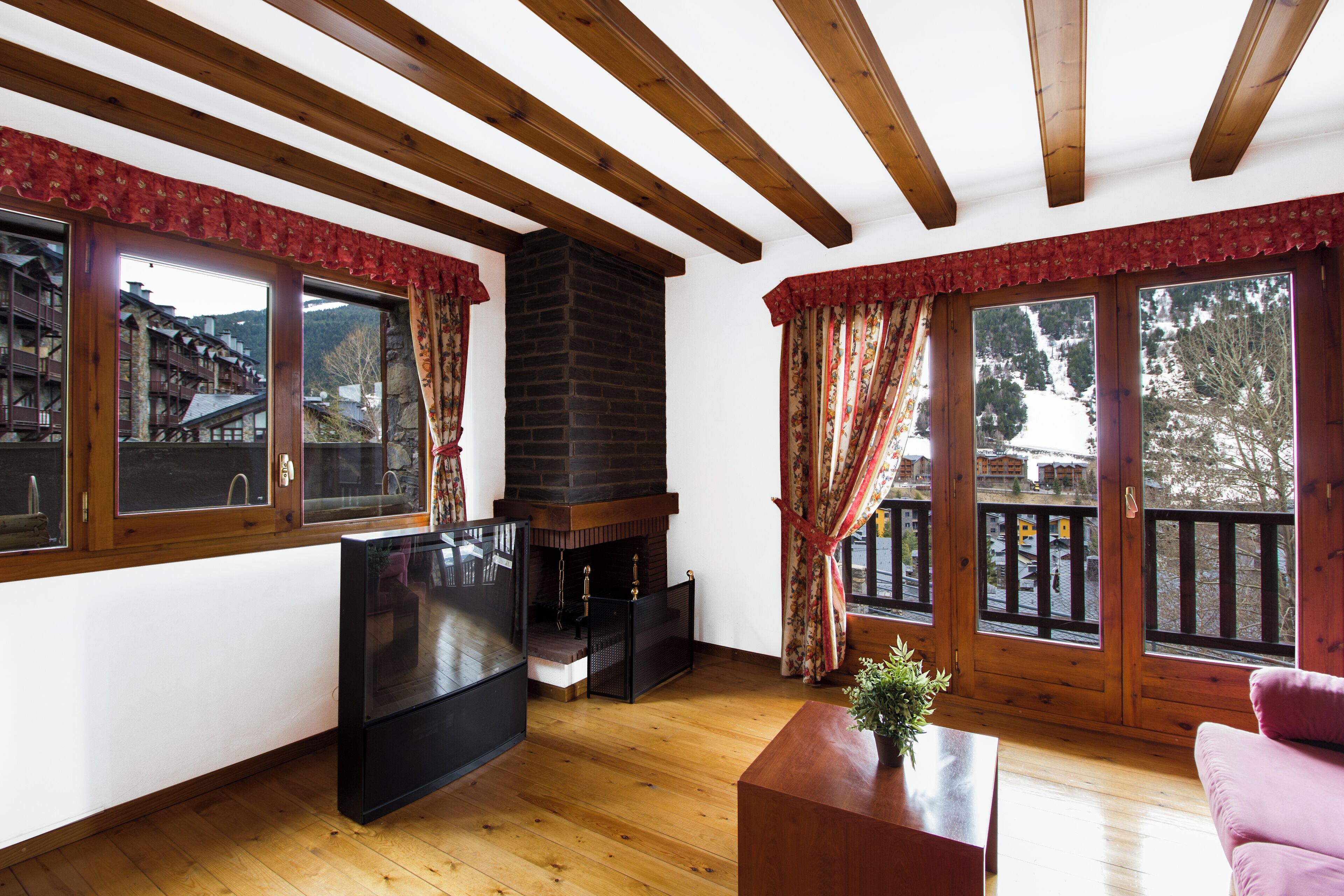 A cozy living room with wooden beams, a fireplace, large windows, and a pink sofa.
