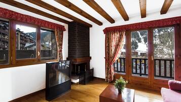 Una sala de estar acogedora con vigas de madera, chimenea, ventanas amplias y un sofá rosa.