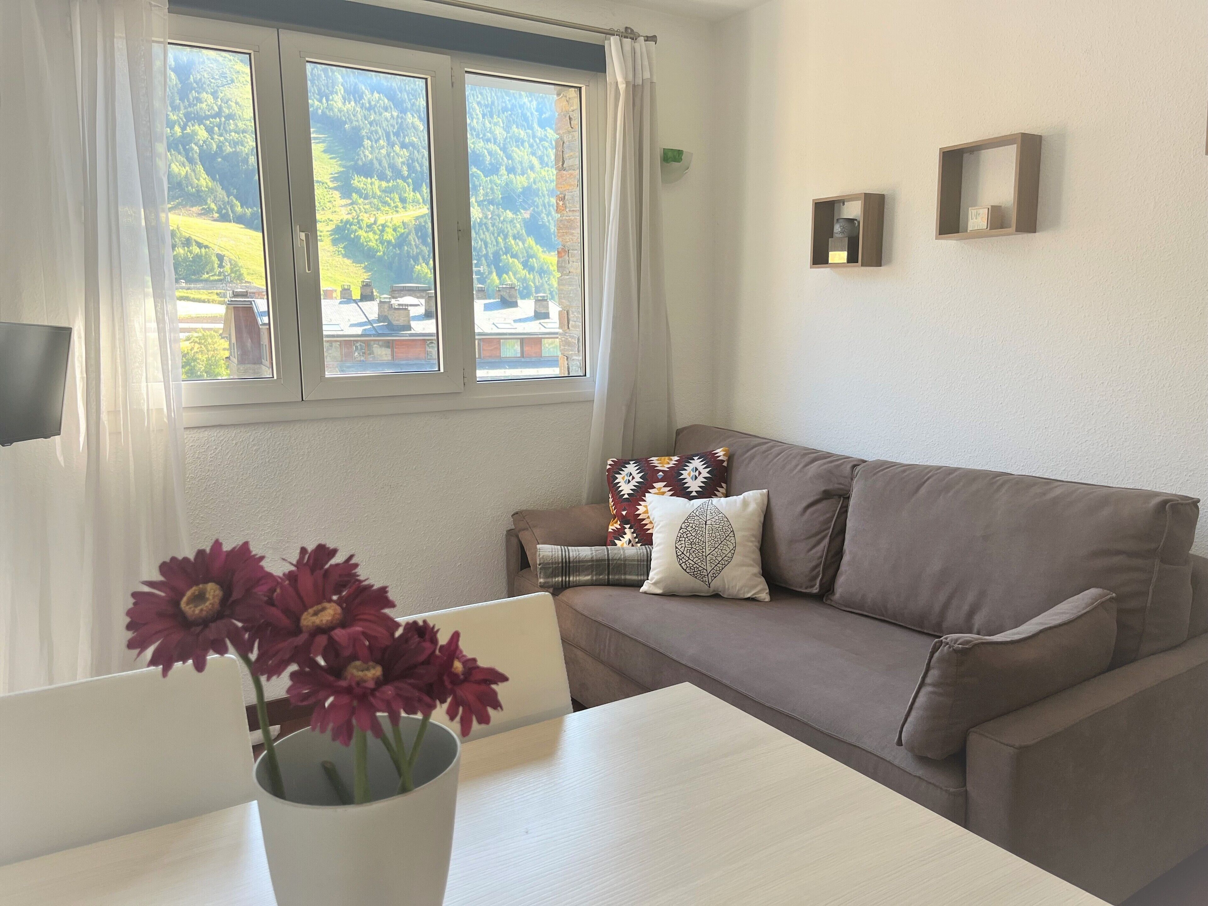 A living room with a sofa, a table, and a window with a view of a green landscape.