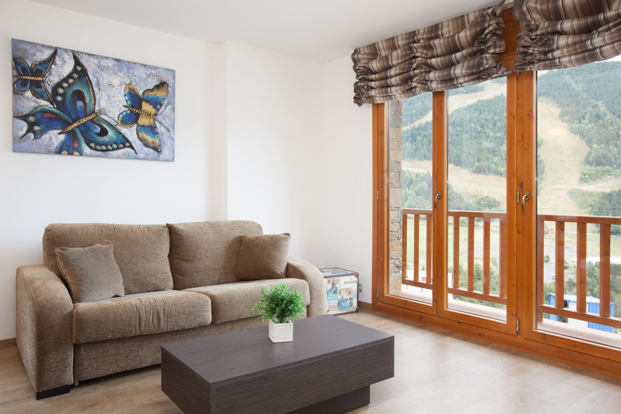 A living room with a beige sofa, a dark wooden coffee table, and a painting of butterflies.