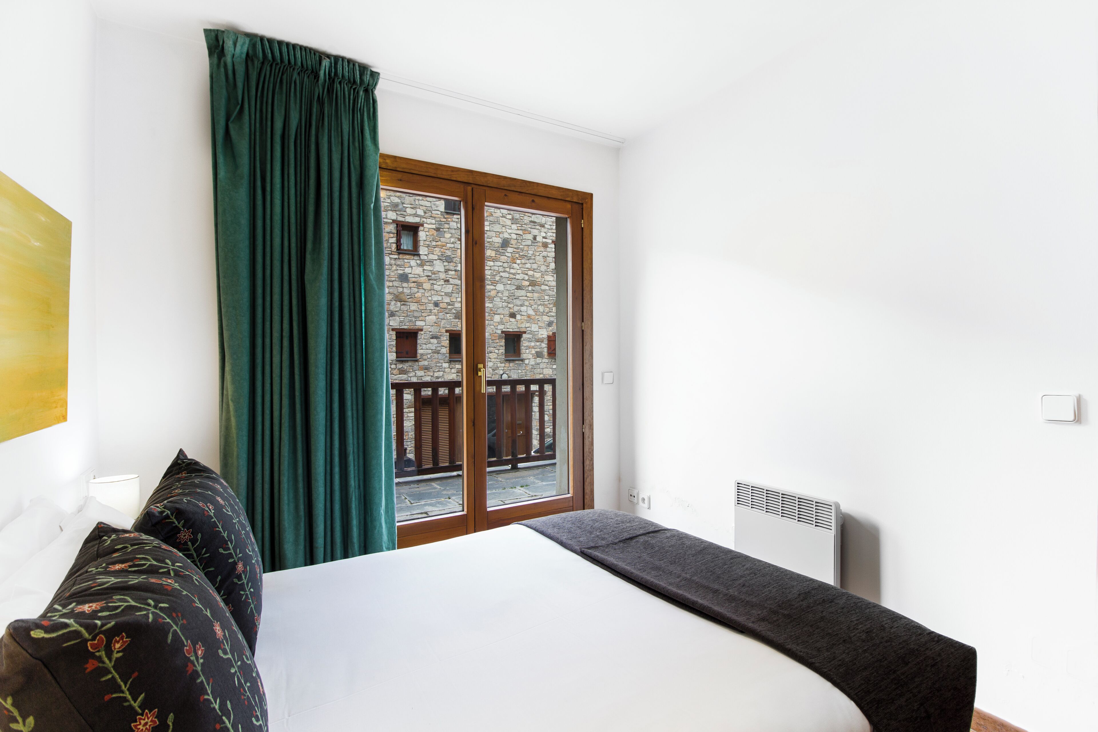 Habitación de hotel con cama, ventana con vista a un edificio, radiador y cortina.