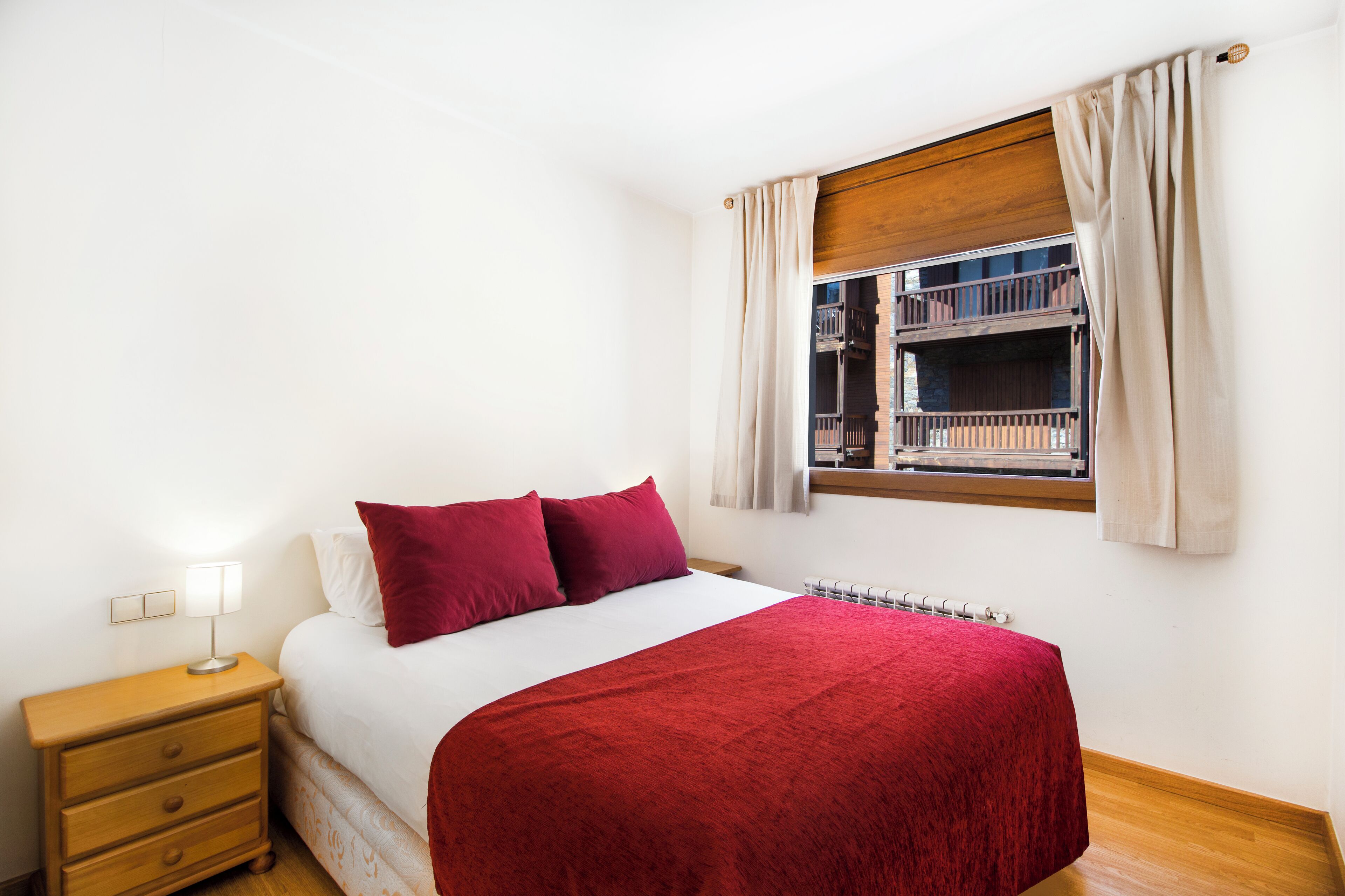 Une chambre à coucher comprenant un lit, une table de chevet, une fenêtre avec des rideaux et donnant sur un balcon extérieur.