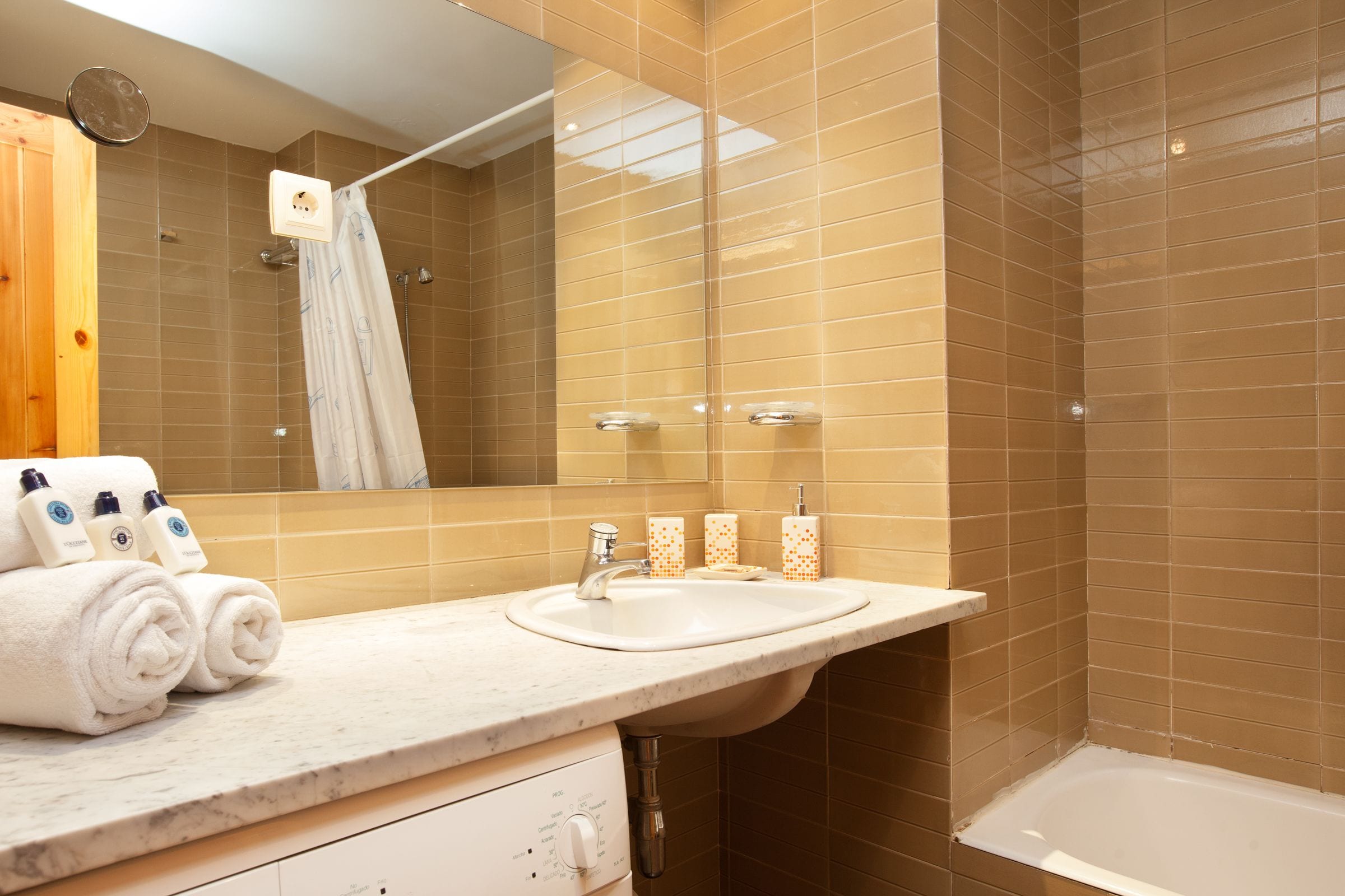Un baño con lavamanos, espejo y ducha. Hay toallas y artículos de aseo en la encimera.