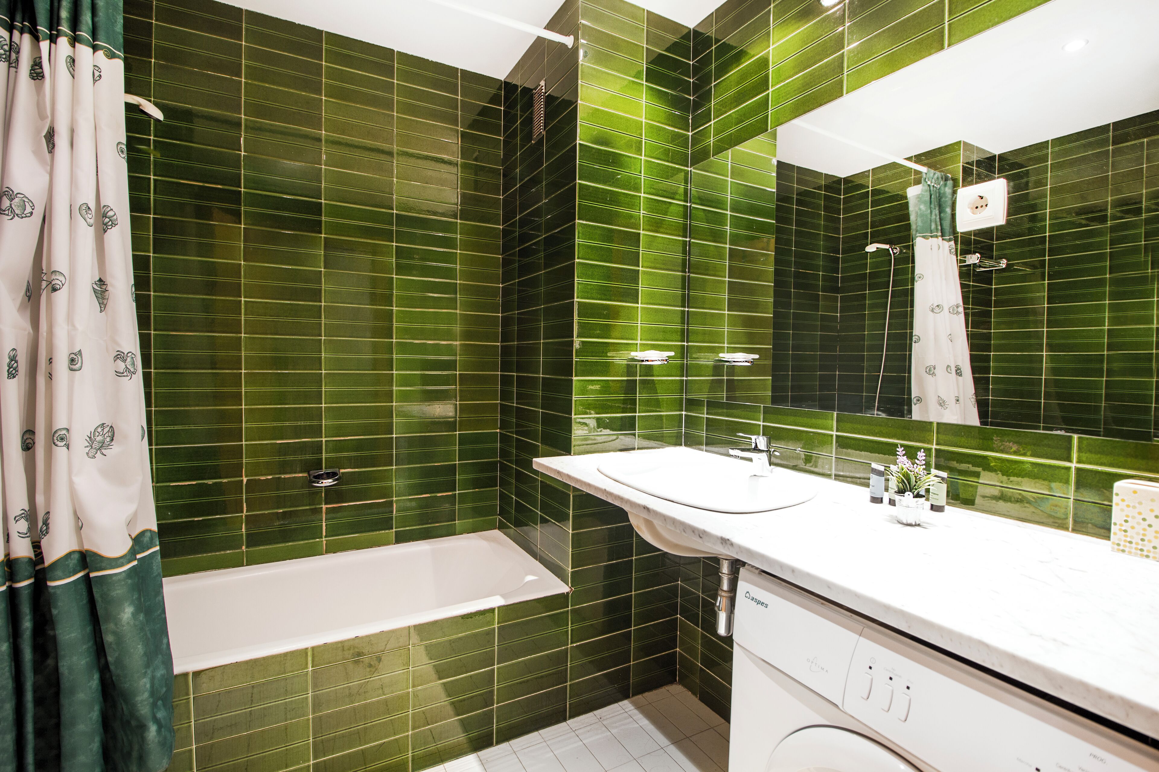 A bathroom with green tiled walls, a white bathtub, a sink, and a mirror.