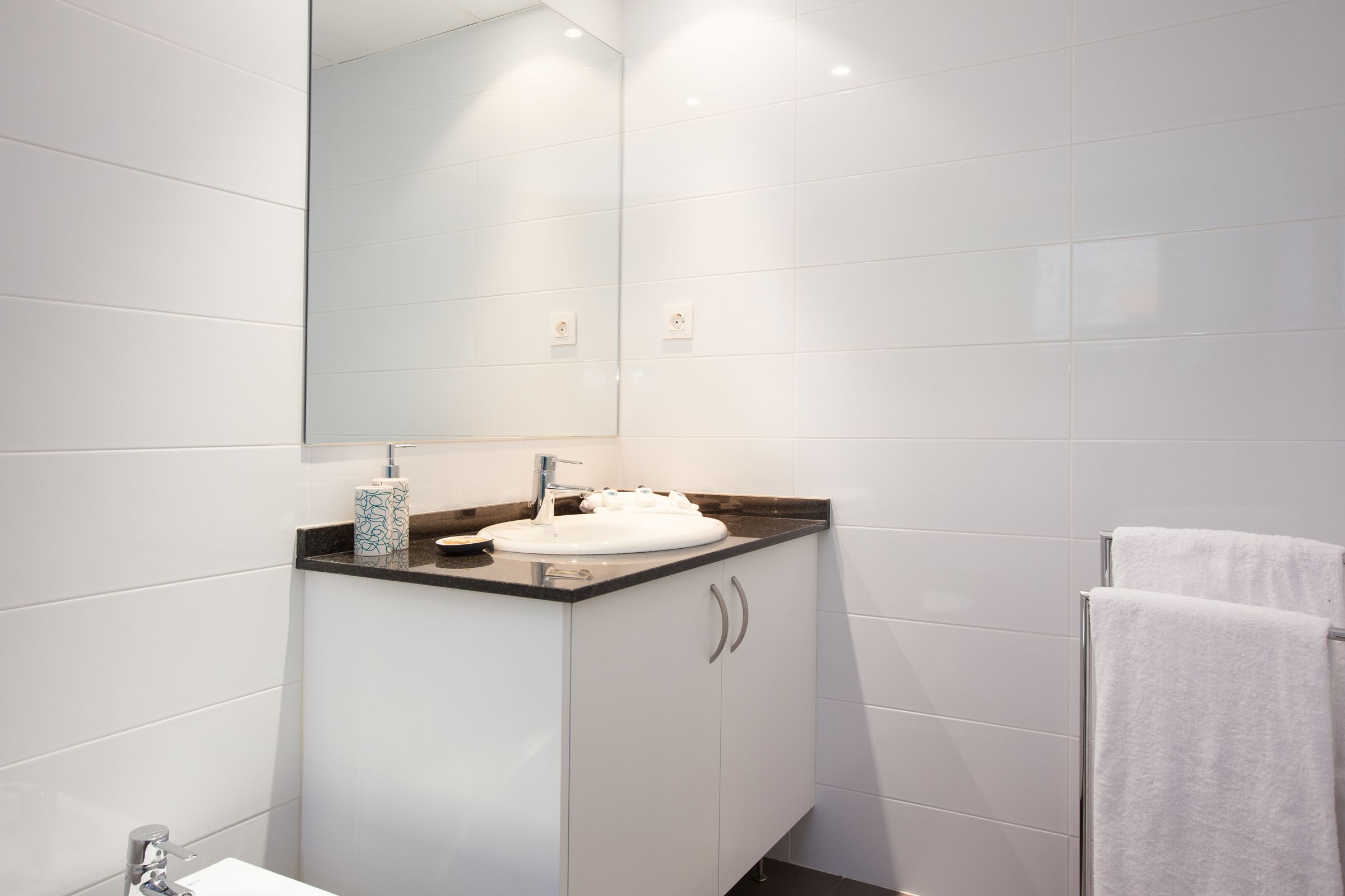 A modern bathroom with a white sink, a mirror, and a towel rack.