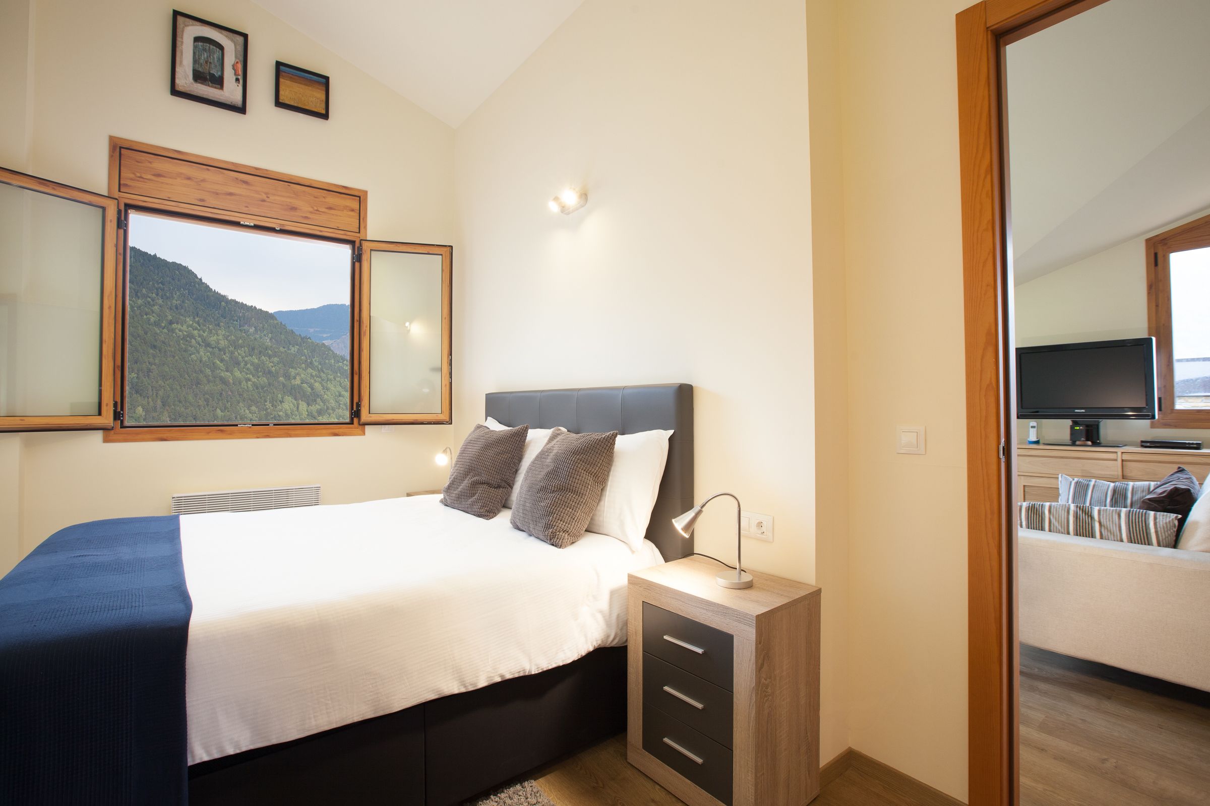 A bedroom with a bed, bedside table, and a view of a mountainous landscape through a window.
