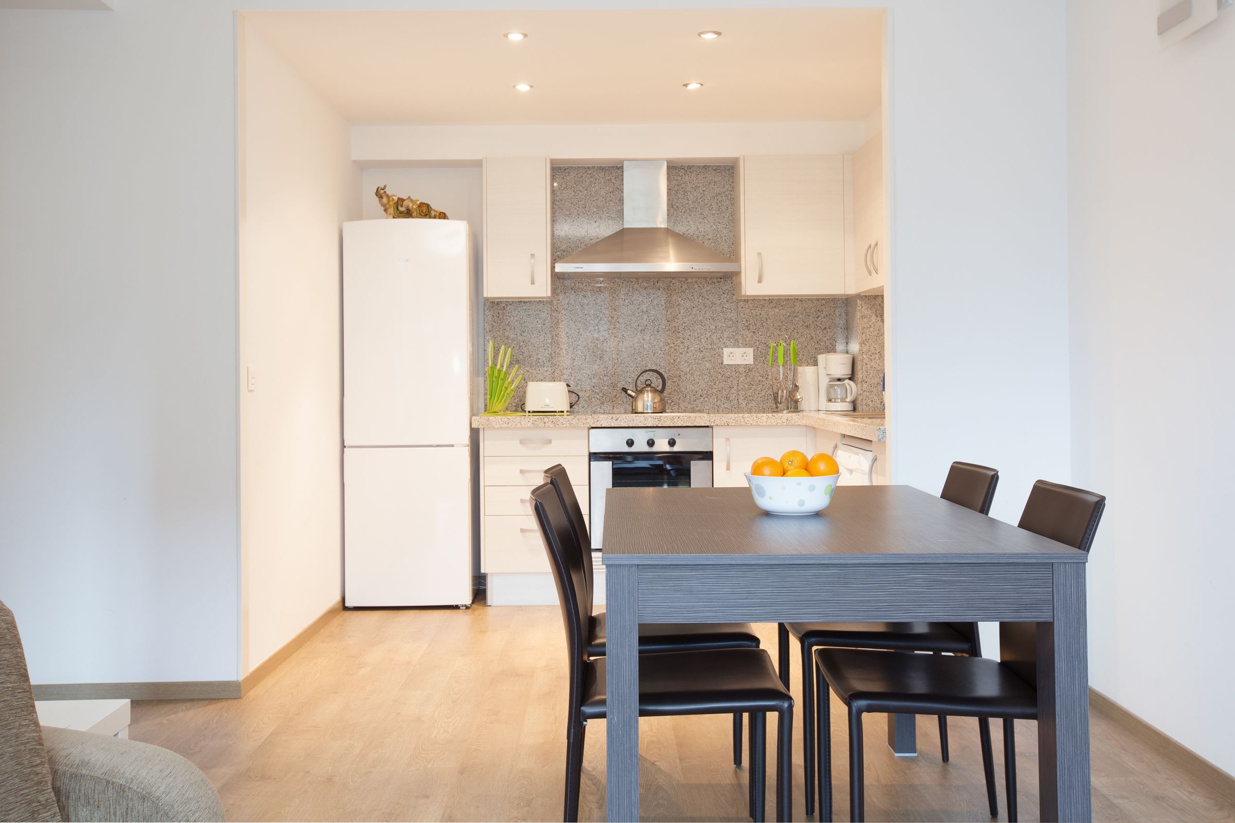 A modern kitchen with white cabinets, a stainless steel range hood, and a dining table with chairs.