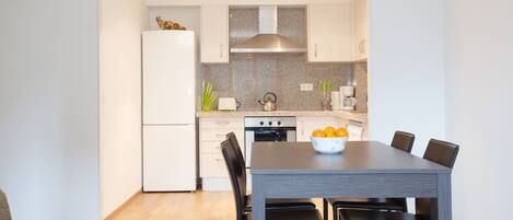 A modern kitchen with white cabinets, a stainless steel range hood, and a dining table with chairs.