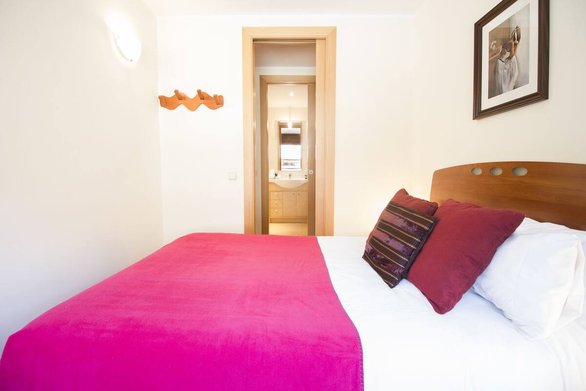 A hotel room with a bed, a wooden headboard, a mirror, and a door leading to a bathroom.