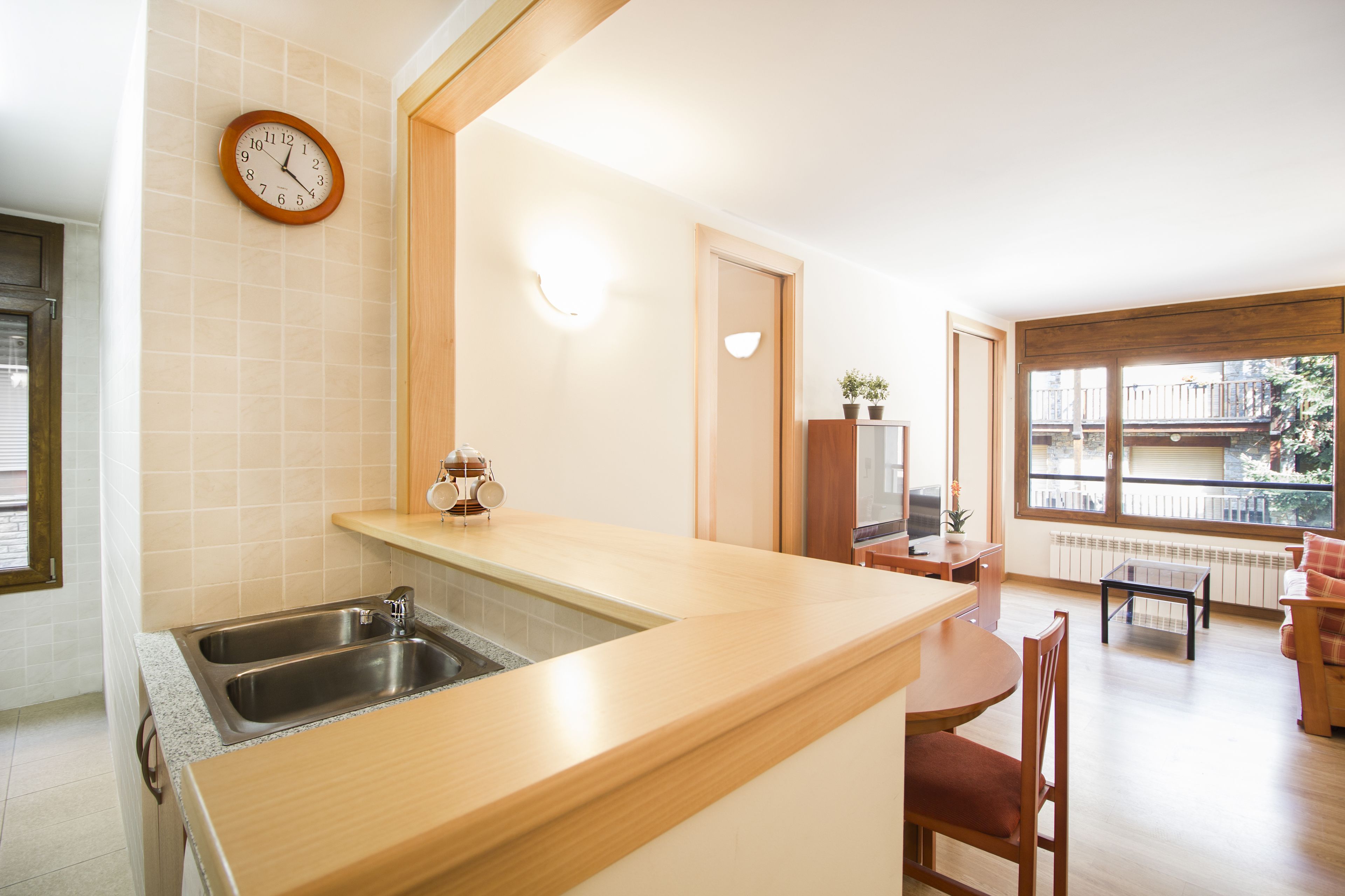Cucina con piano di lavoro in legno, lavello in acciaio inossidabile e orologio a parete.