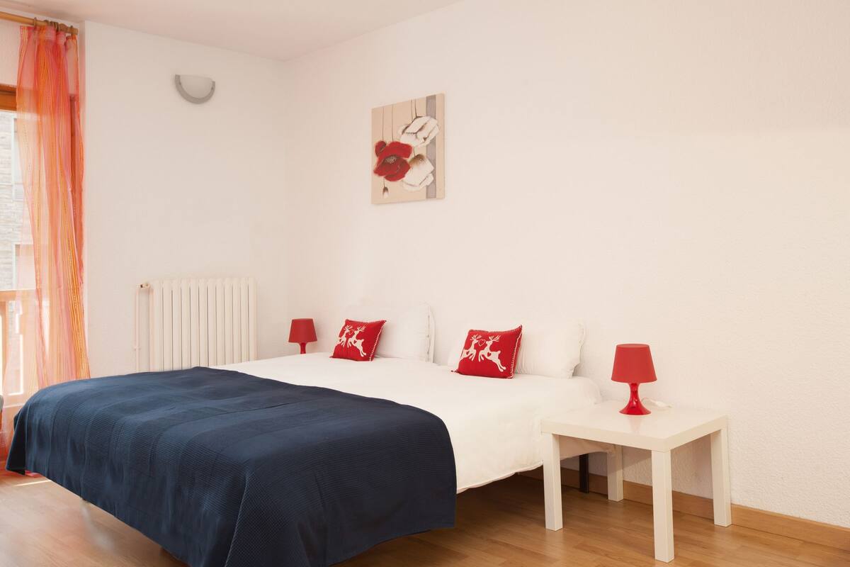 A neatly arranged bedroom with a large bed, a bedside table with a lamp, and a wall-mounted artwork.