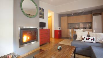 A modern living room with a fireplace, a kitchen area, and a dining space.