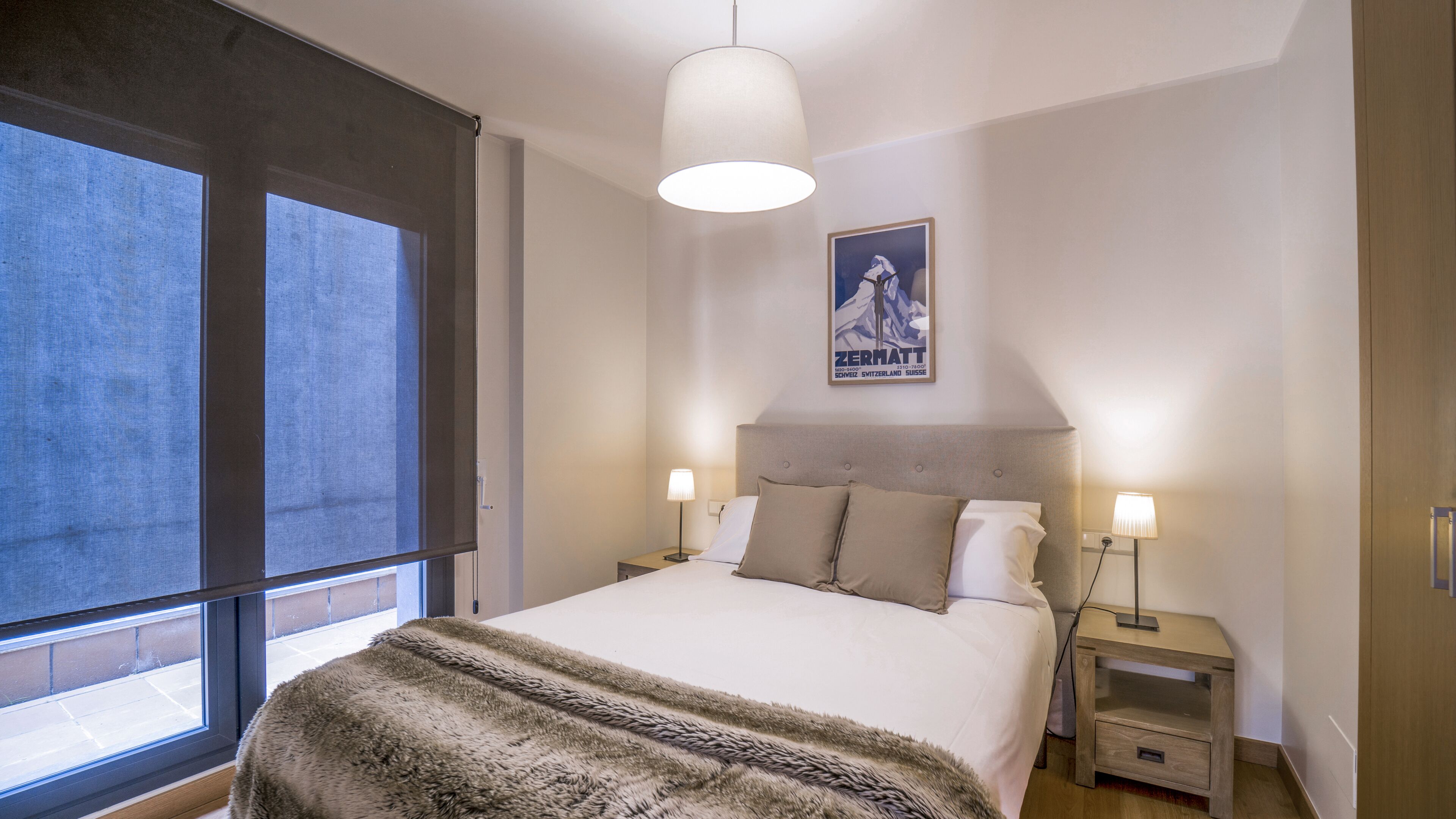 Un dormitorio con una cama grande, dos mesitas de noche con lámparas, una ventana con vistas y un cartel en la pared.