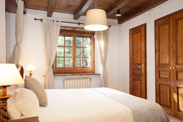 A bedroom with a bed, a window with curtains, a radiator, wooden doors, and a hanging light fixture. - Tarter Mountain Suites (El Tarter)