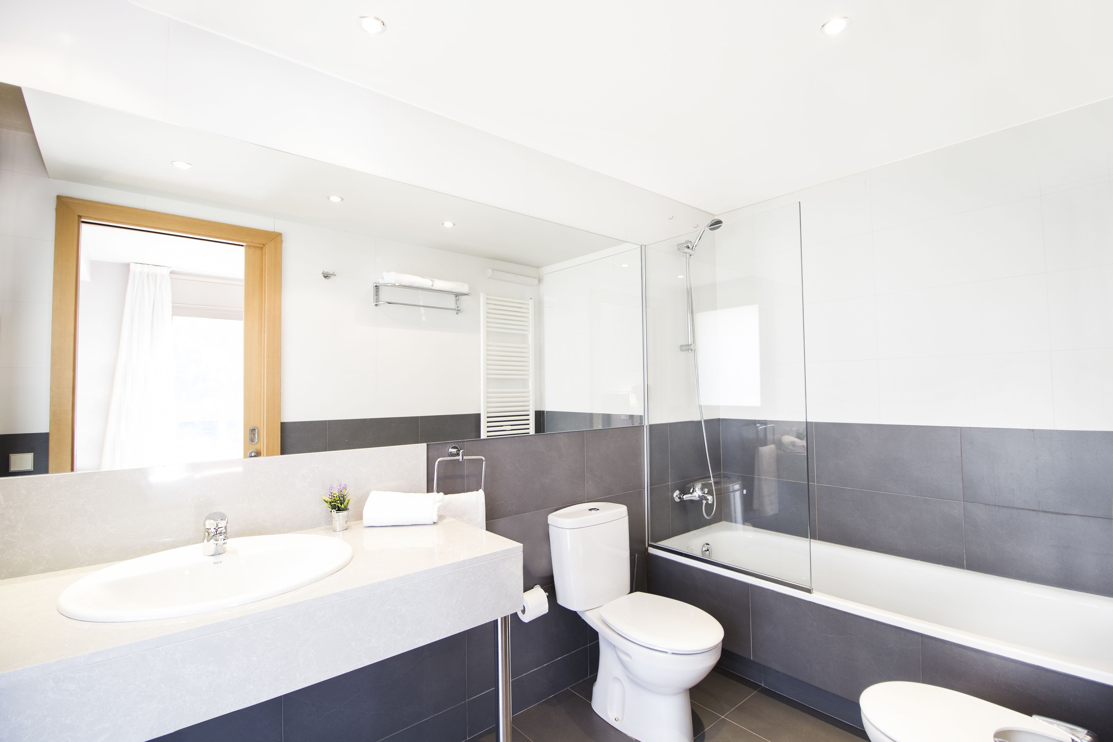 A modern bathroom with a large mirror, a sink, a toilet, and a bathtub.