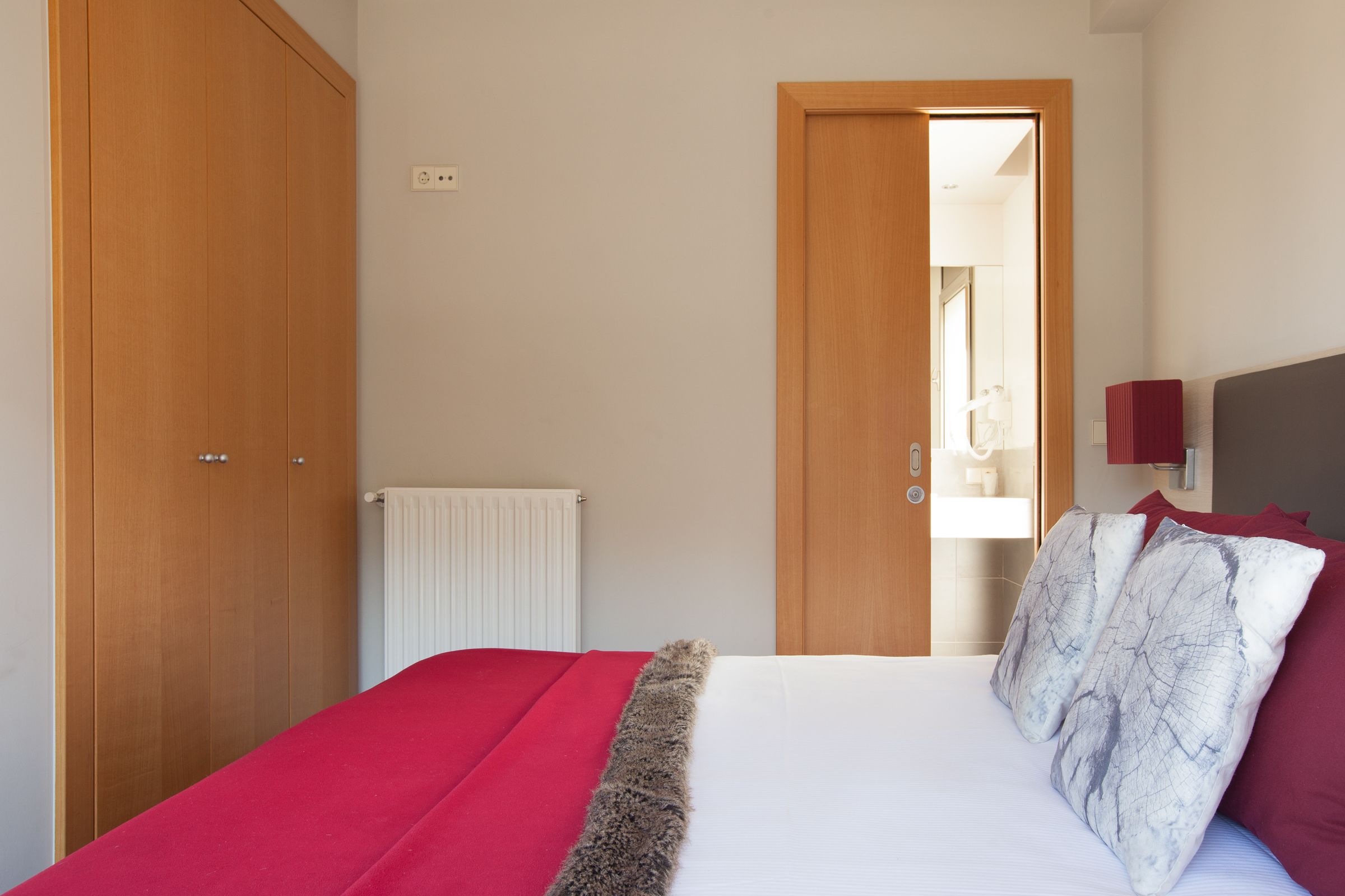 Un dormitorio con cama, un armario de madera, un radiador y una puerta que da a otra habitación.