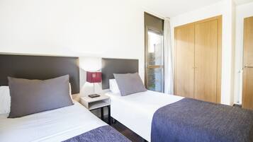 A hotel room with two beds, a nightstand with a lamp, and a wooden wardrobe.