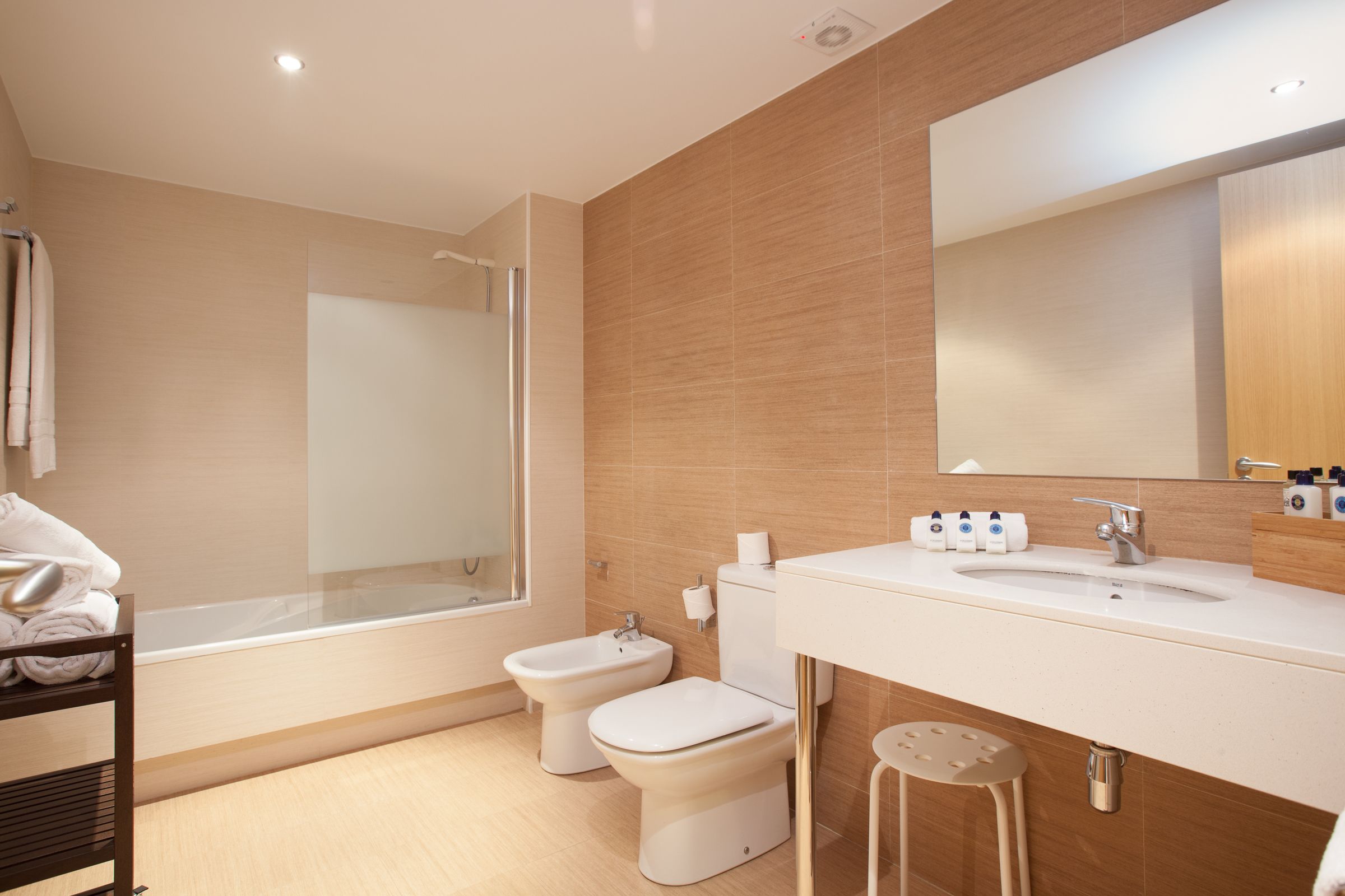 A modern bathroom with a bathtub, two toilets, a sink, and a mirror.