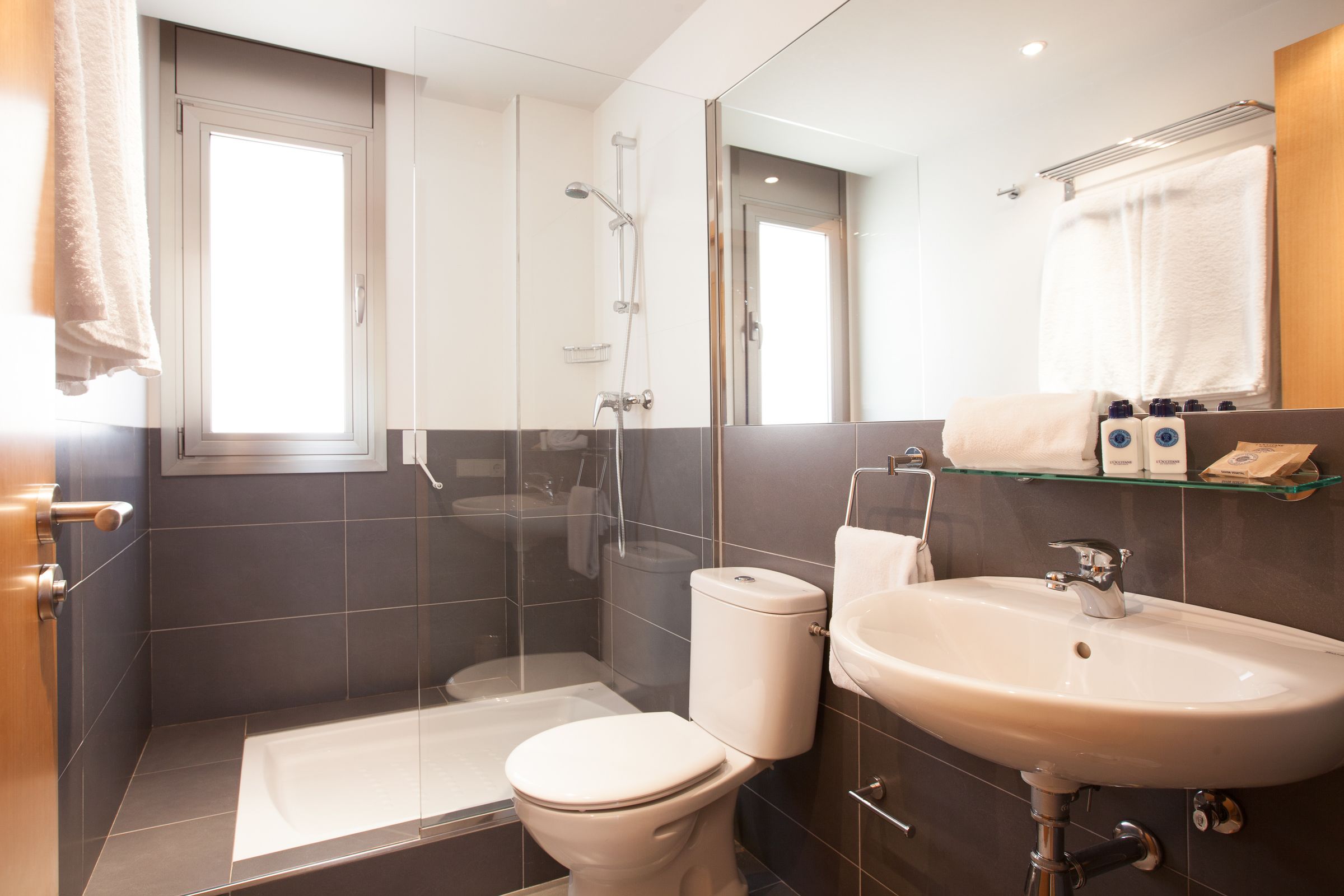 A modern bathroom with a glass-enclosed shower, a white toilet, a sink, and a mirror.