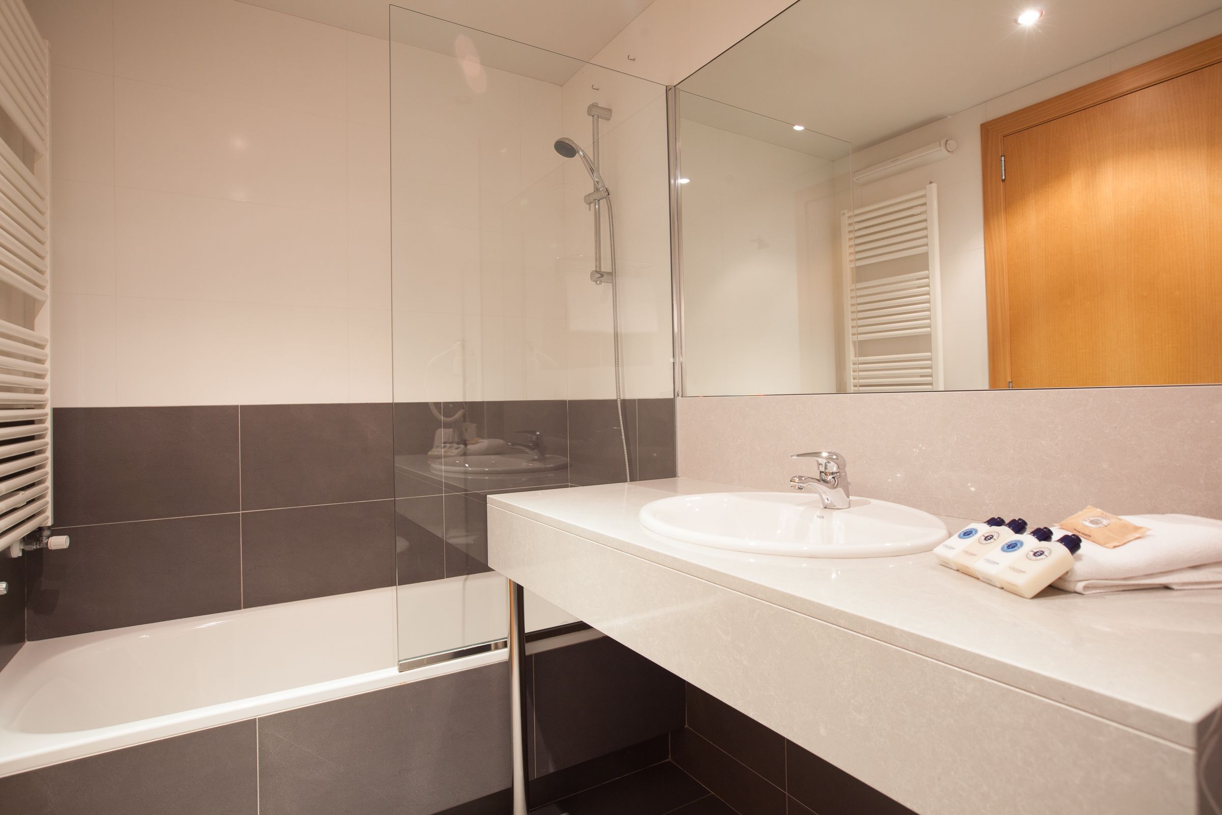 Ein modernes Badezimmer mit einer gläsernen Duschkabine, einem weißen Waschbecken und einer Holztür.