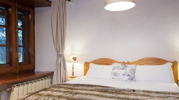Une chambre à coucher avec une tête de lit en bois, un lit recouvert de linge de lit blanc, un plaid en fourrure, une lampe de chevet avec un abat-jour en forme de cœur et une fenêtre avec des rideaux.