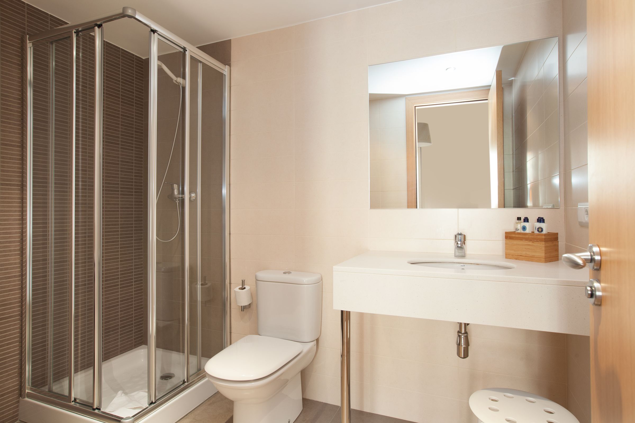 Un baño moderno con ducha de vidrio, inodoro, lavabo con espejo y un caja de almacenamiento de madera.