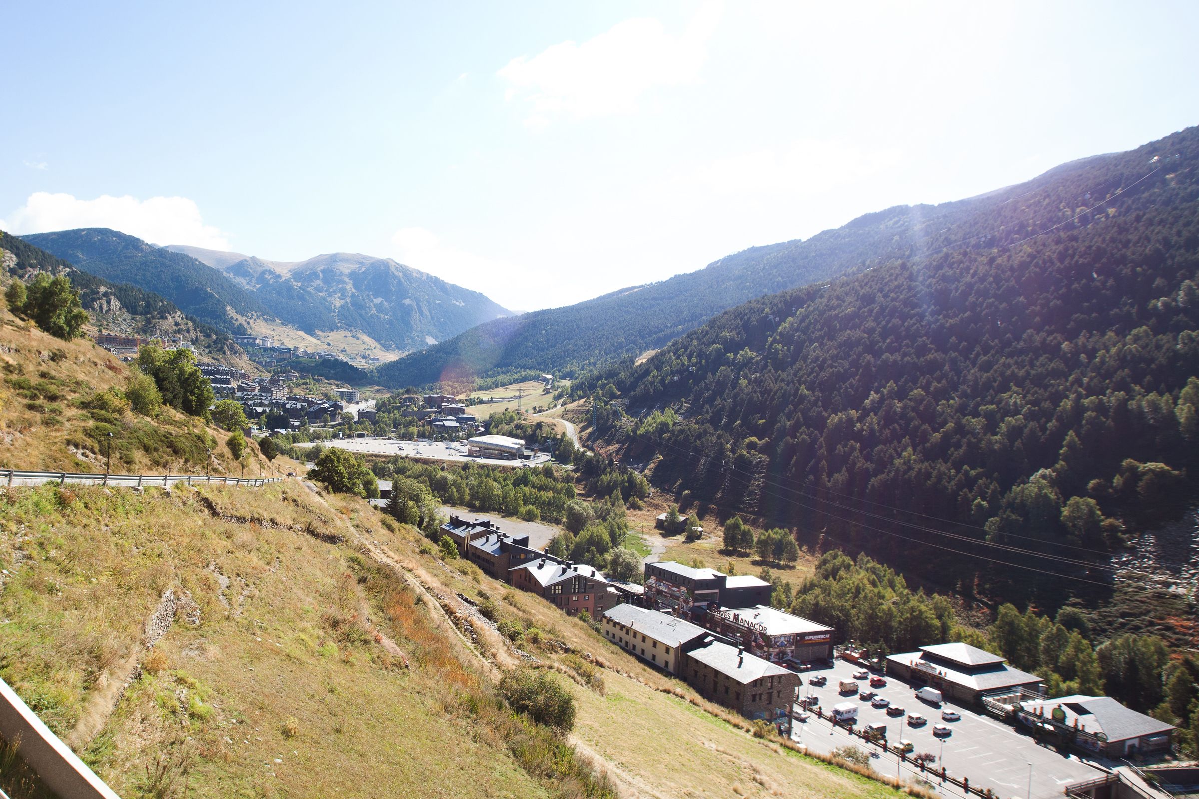 A mountainous landscape with a small town featuring several buildings, a parking lot, and a river.