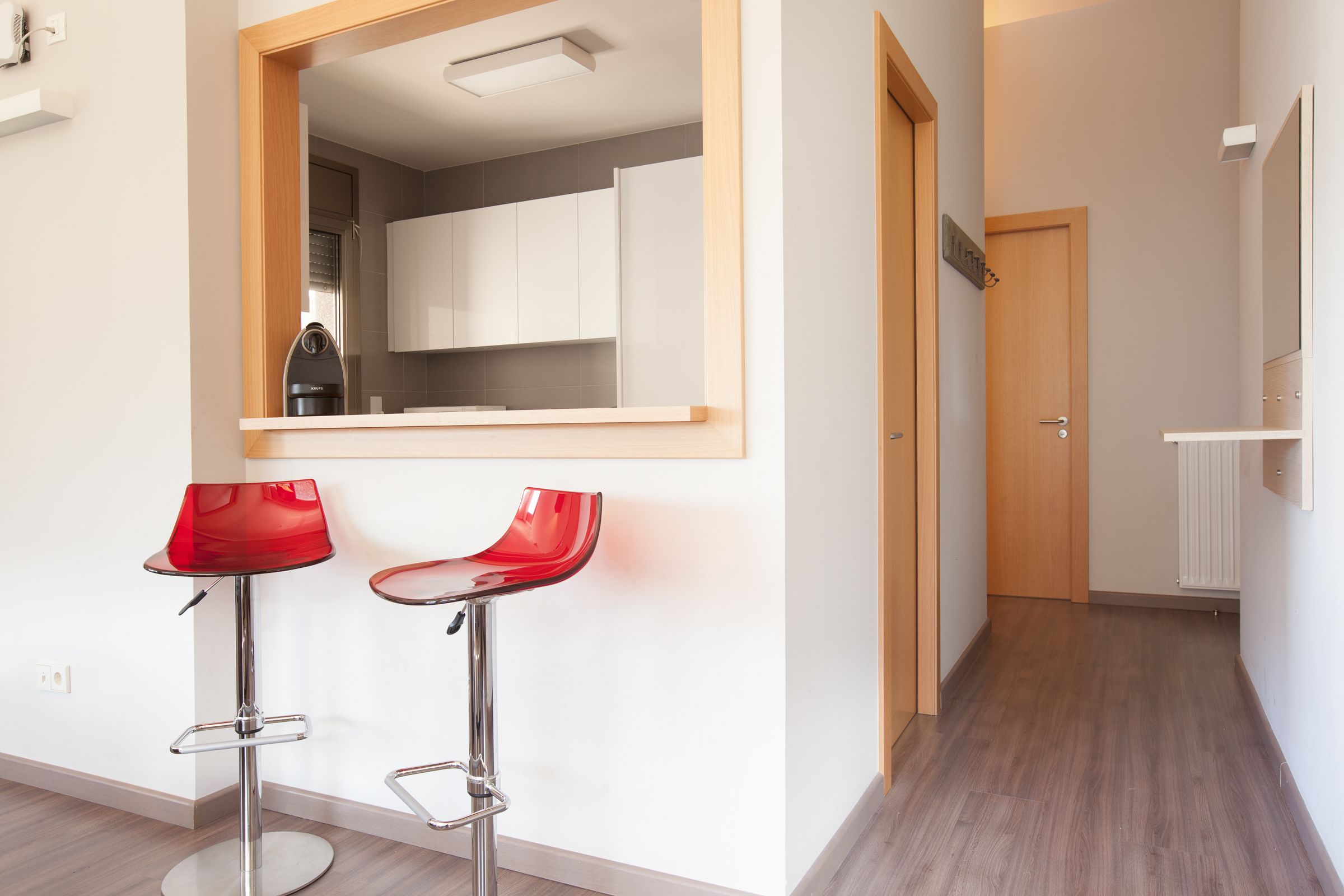 A modern kitchen with white cabinets, a wooden door, and a red bar stool.