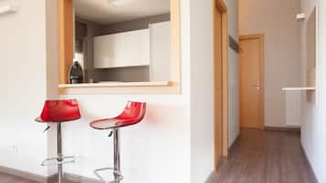 A modern kitchen with white cabinets, a wooden door, and a red bar stool.