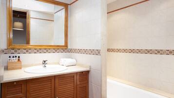 Un baño con tocador de madera, lavamanos, espejo y bañera.