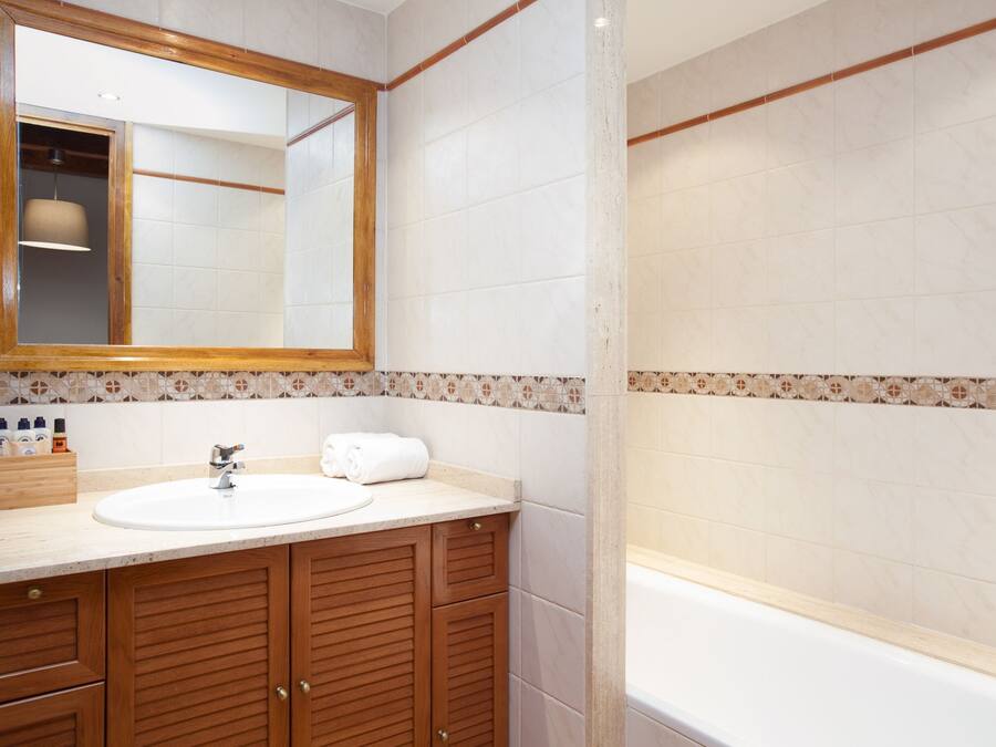 Un baño con tocador de madera, lavamanos, espejo y bañera.