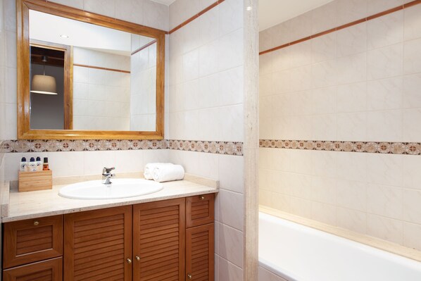 A bathroom with a wooden vanity, a sink, a mirror, and a bathtub. - Tarter Mountain Suites (El Tarter)