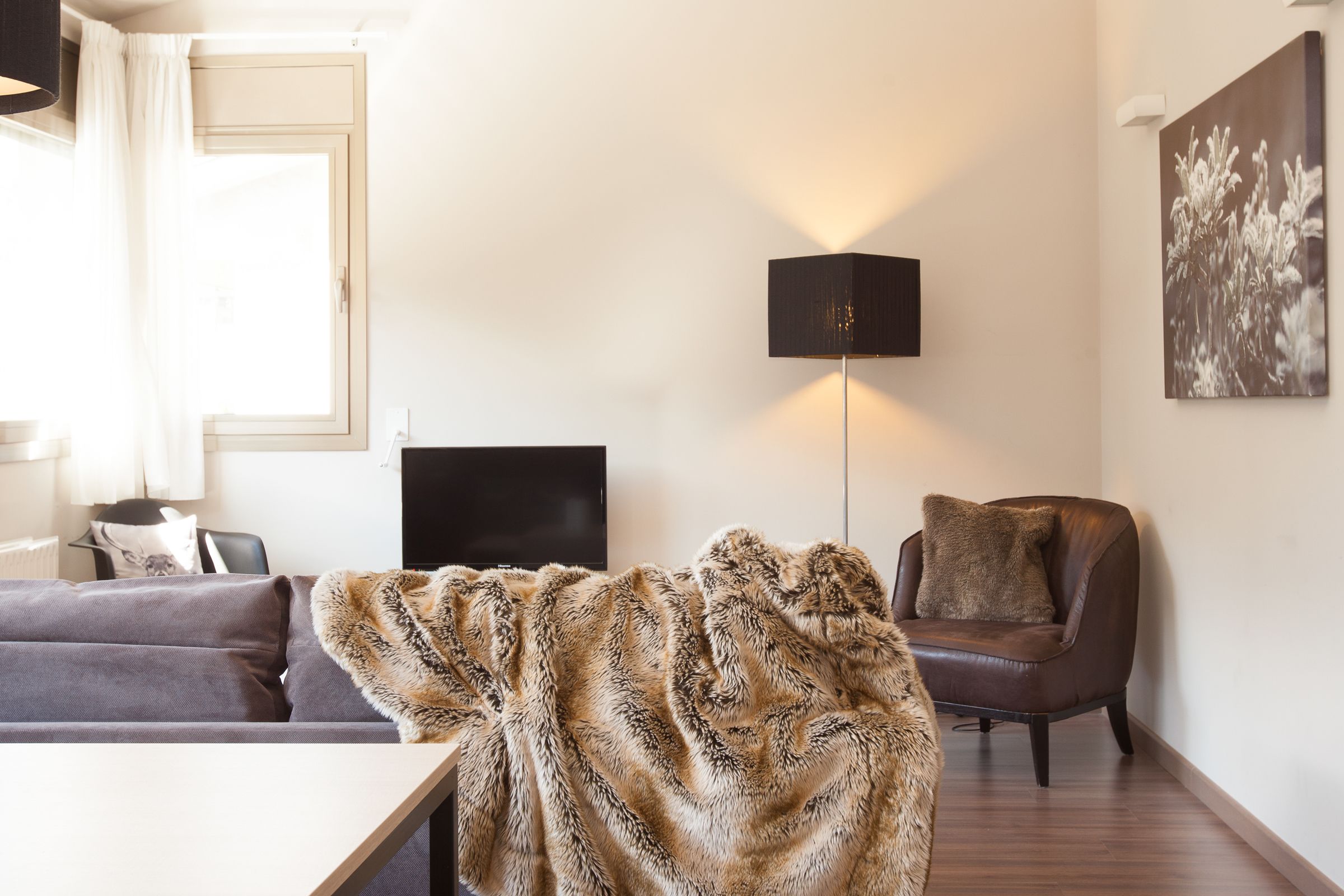 Una sala de estar moderna con sofá, sillón, televisor de pantalla plana, lámpara y un cuadro en la pared.