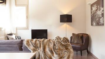 Una sala de estar moderna con sofá, sillón, televisor de pantalla plana, lámpara y un cuadro en la pared.
