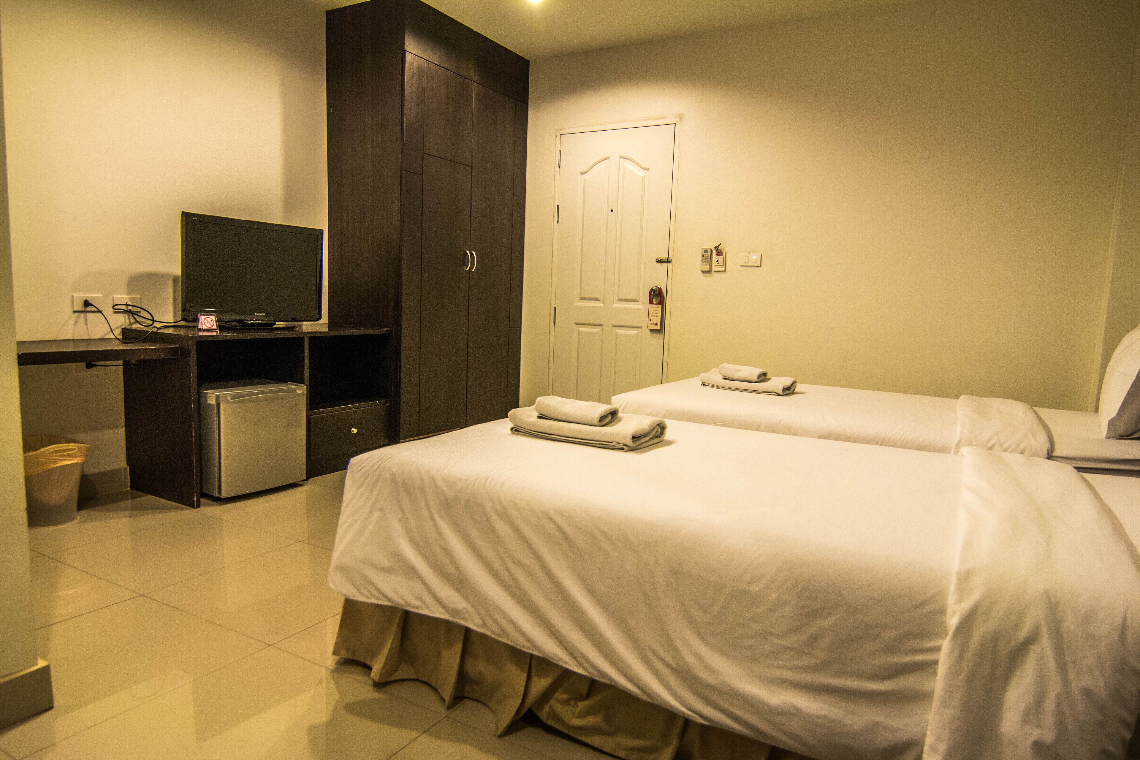 Habitación de hotel con dos camas, un escritorio con televisor, un refrigerador pequeño y una puerta con cerradura.