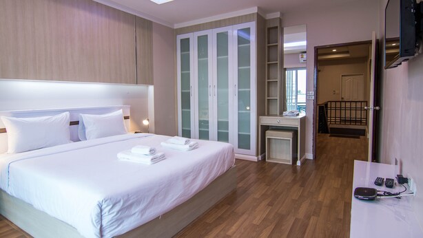 Una habitación de hotel moderna con una cama grande, un tocador con espejo, un armario con puertas de cristal y un televisor fijado a la pared.