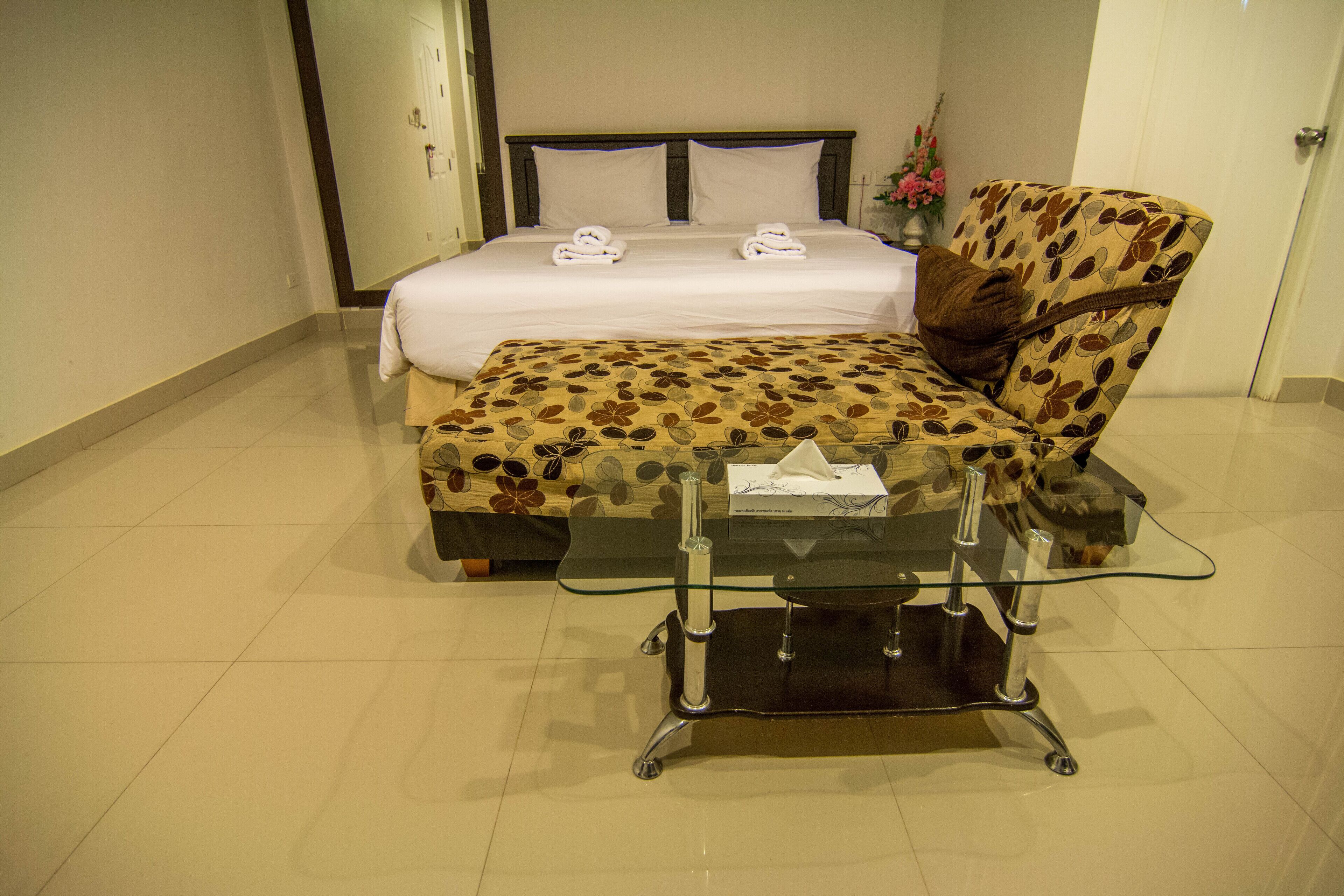 A hotel room with a bed, a chair, and a small table with a tissue box.