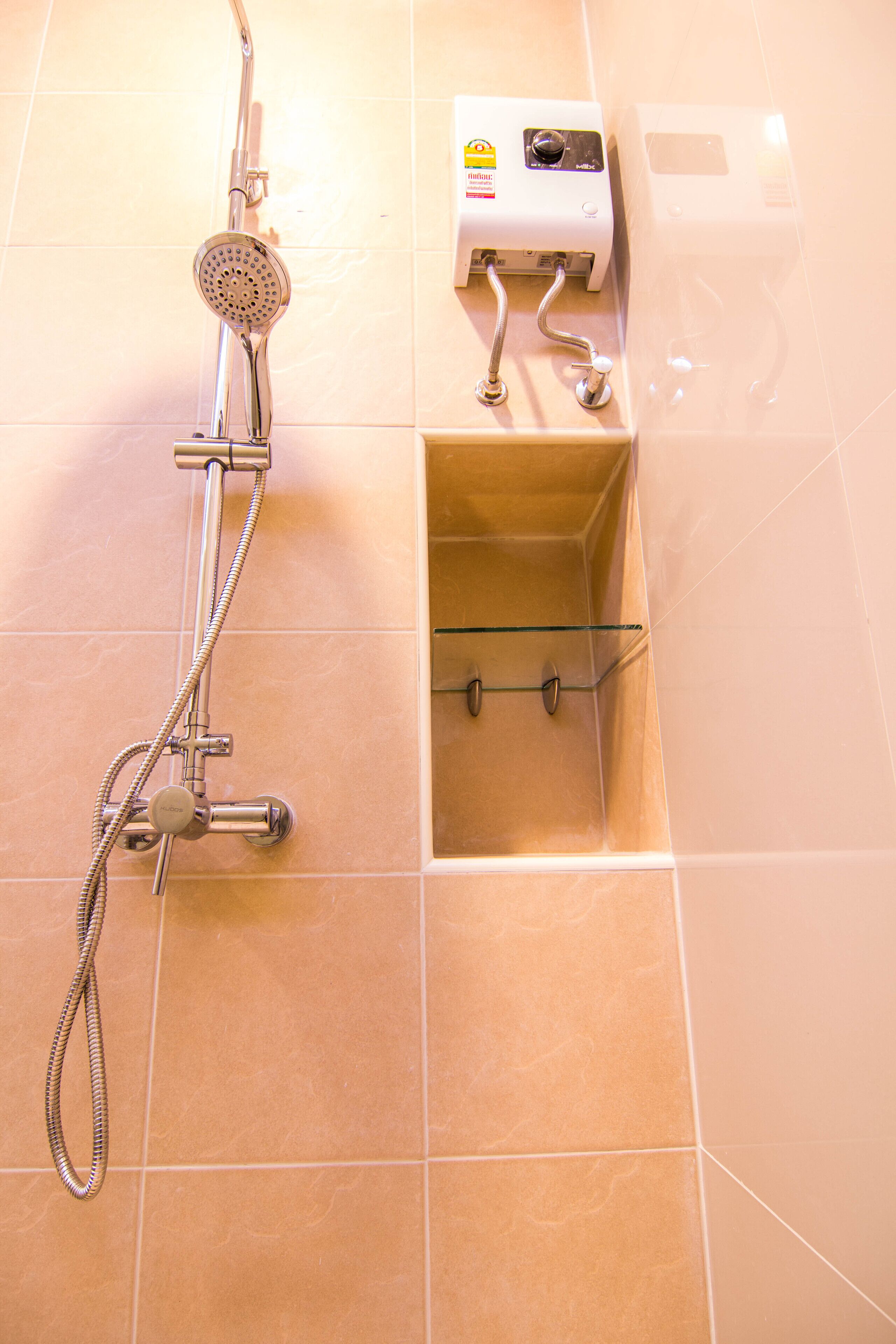 A shower with a handheld showerhead, a wall-mounted control panel, and a glass shelf.