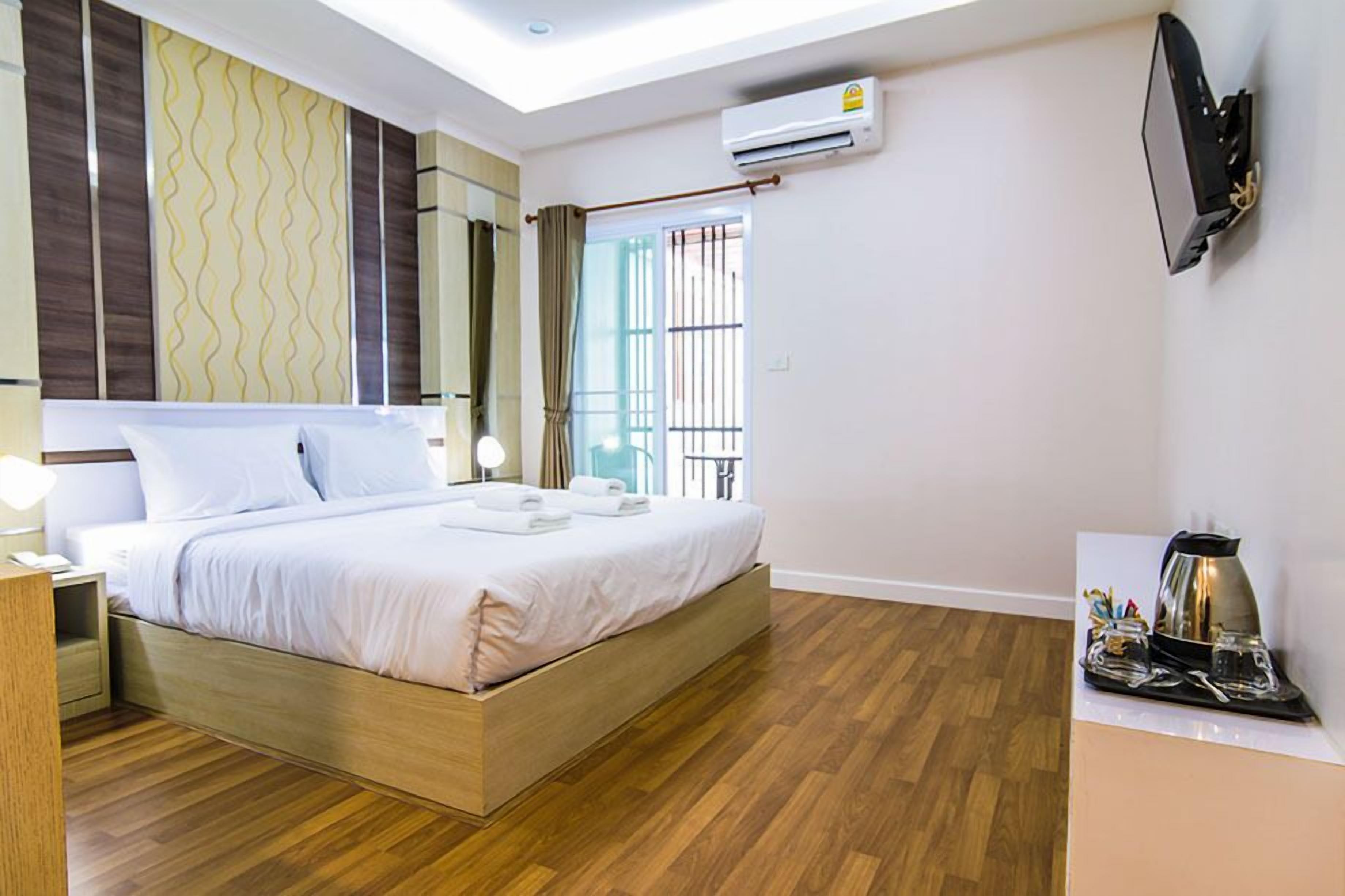 Una habitación de hotel moderna con una cama de madera, un televisor de pantalla plana, un equipo de aire acondicionado y una pequeña mesa con una tetera y tazas.